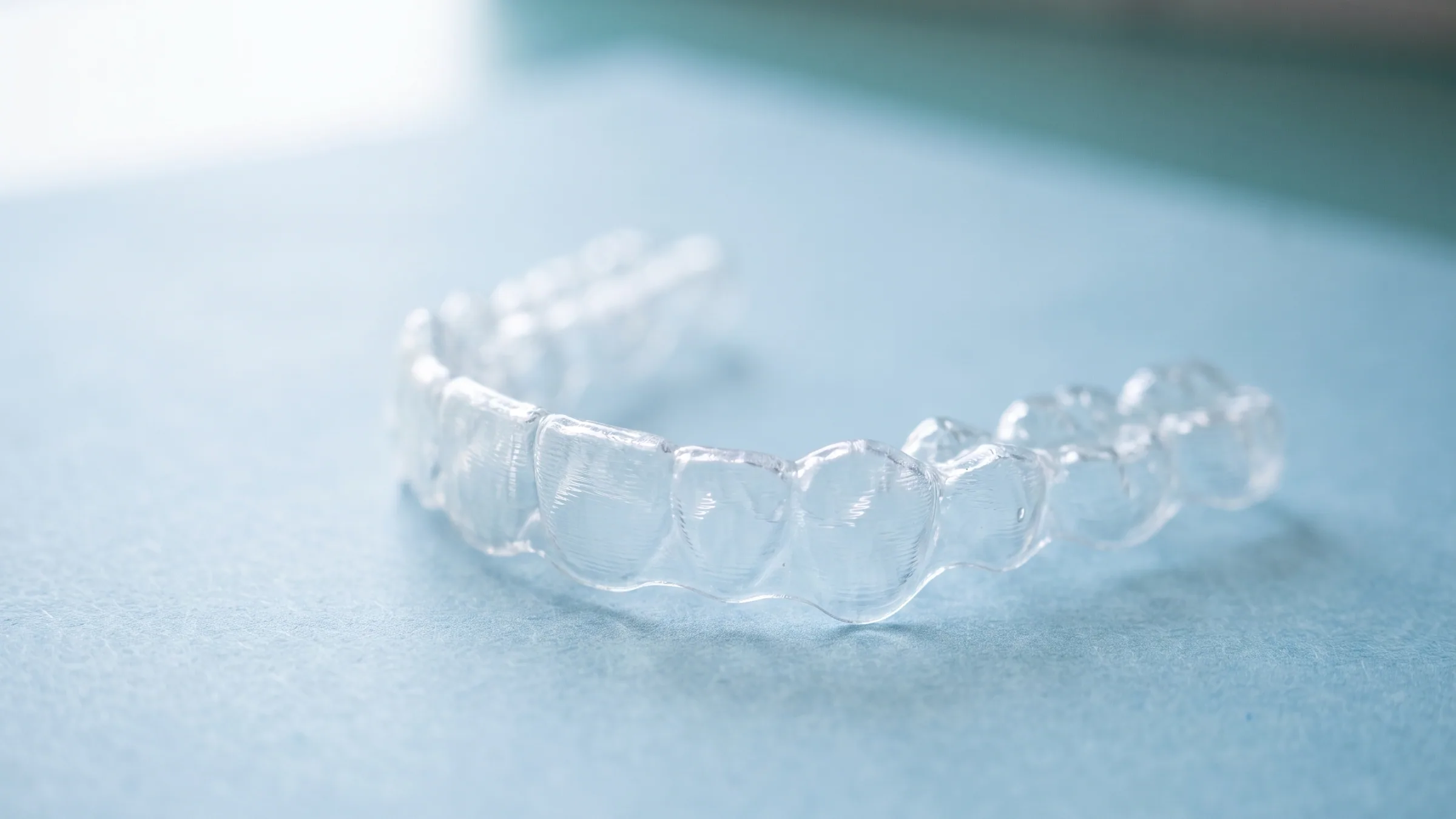 Concept illustration: a clear plastic aligner tray resting on a pale blue paper surface in soft window light