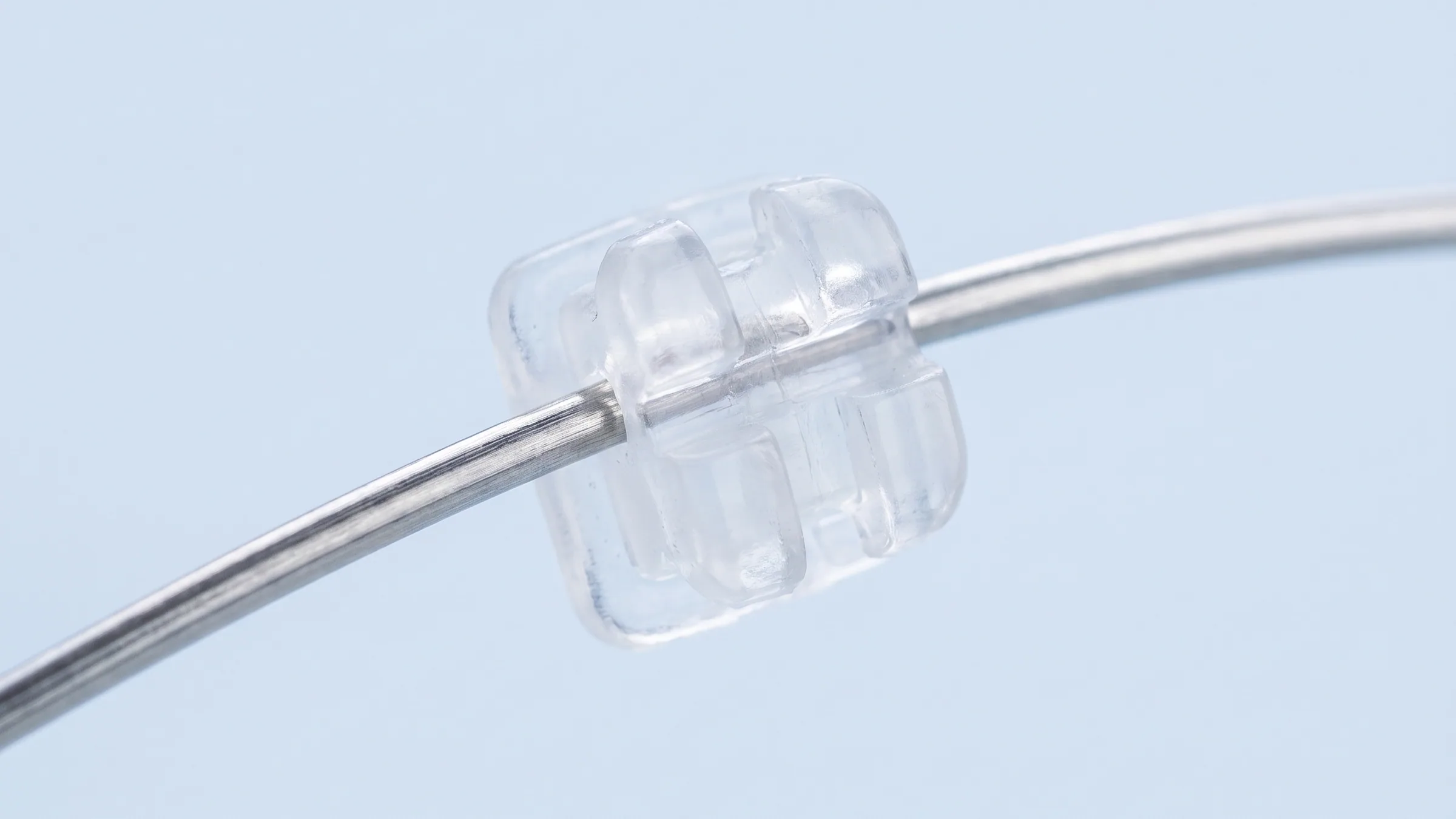 Concept illustration: a clear ceramic bracket seated on a thin stainless steel archwire against a pale blue background