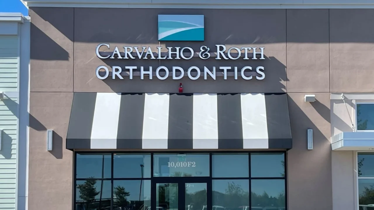 Storefront of the Northborough Crossing office with the lit Carvalho & Roth Orthodontics sign and a striped awning